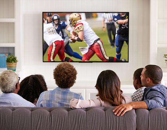 A family gathered on the couch watching a football game on TV