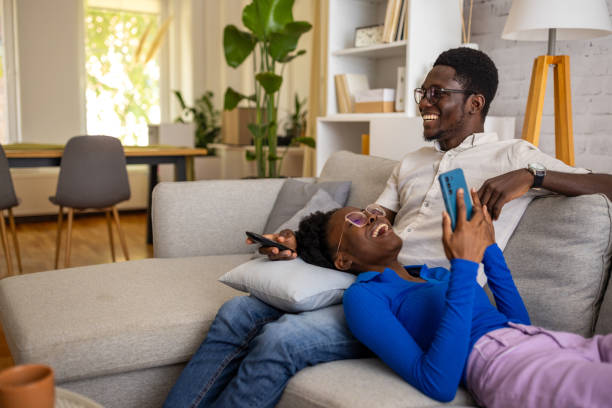 Two people on a couch, one watching TV while the other uses a phone
